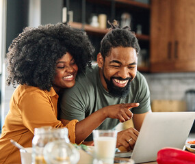 Happy young afro american couple having fun preparing food and looking for recipes online using a laptop in kitchen