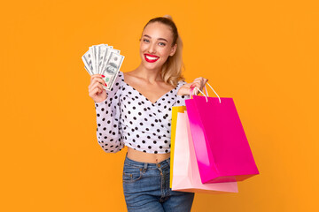 Commerce Concept. Portrait of smiling young lady holding bunch of cash money fan and shopping bags...