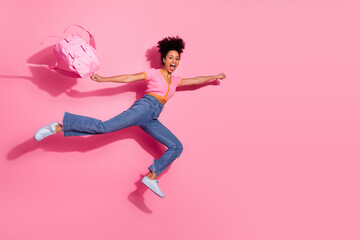 Energetic young woman leaping joyfully with a pink backpack on a vibrant pink background showcasing...