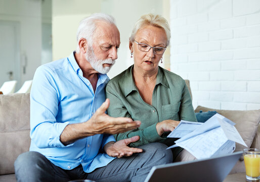 Senior couple checking bills and calculating expenses using a laptop at home, debt taxes concept, worried married elderly couple