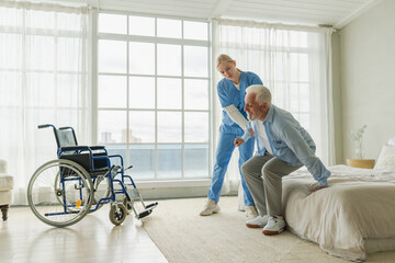 Rehabilitation healthcare. Physiotherapist nurse helps old man patient in wheelchair stand up...