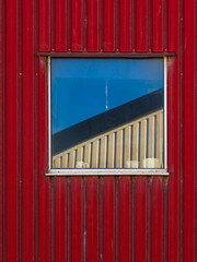 Reflections of industrial architecture in a Swedish building window against a bright blue sky