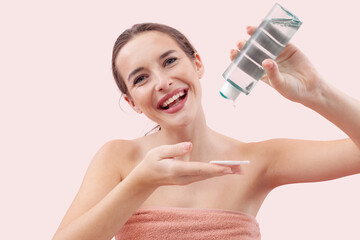 Smiling young woman pouring micellar water onto a cotton pad before cleansing her face. Skincare...
