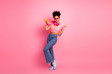 Stylish young woman with skateboard posing confidently on a pink background, showcasing trendy...