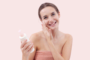 Smiling young woman cleansing her face with cotton pad and micellar water. Skincare routine, makeup...