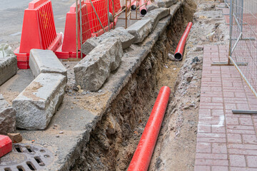 Road repairs, pipe, pile of sand. Red and white plastic barriers blocking the road.