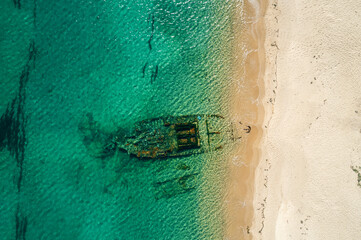 Shipwreck partially submerged in clear turquoise water along a sandy beach during daylight