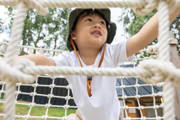 Asian Happy playful child climbing rope net outdoors, smiling joyfully and exploring adventure...