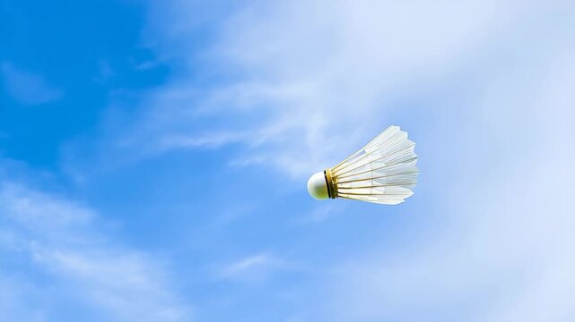 A white badminton shuttlecock is flying in the air. The shuttlecock is white and has a black stripe