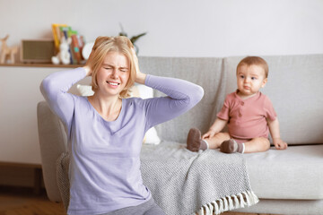 Postnatal depression concept. Stressed blonde woman young mother suffering from headache, sitting...