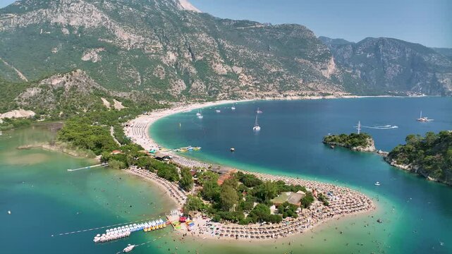 Aerial view capturing tourists lounging on sunbeds and swimming in luminous turquoise waters of oludeniz blue lagoon during vibrant summer day in fethiye, turkey's mediterranean coastline