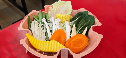 Organic vegetables, arranged in pink bowl placed on red table. Set of healthy vegetables : carrots,...