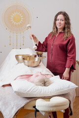Sound therapist performs healing session with Tibetan singing bowls. Client lies relaxed on massage...