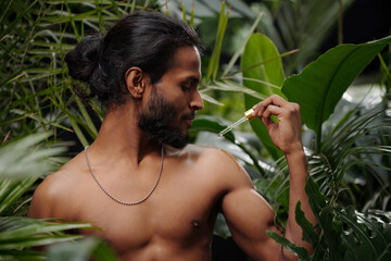 Man applying serum on shoulder standing in lush tropical forest surrounded by various green plants....