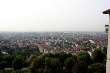 Hazy, elevated view of Bergamo's cityscape with red roofs and numerous trees. Muted atmosphere