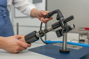 Person holding a black metal device with tubes and stand on a blue surface in a bright room
