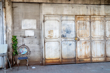 A Worn Urban Building With Multiple Shutted Storefronts And A Parked Car.