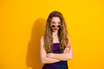 Confident young woman posing with star-shaped sunglasses against a vibrant yellow background, showcasing trendy fashion and a playful attitude.