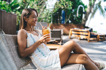 Smiling freelancer enjoying iced tea and moment of joy while working remotely, balancing digital...