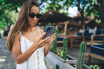Young brunette woman with sunglasses checks phone attentively, representing digital nomad...