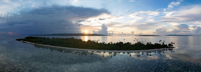 A serene sunrise silhouettes an island within Wakatobi National Park, off the coast of Sulawesi. This area is a popular destination for divers and snorkelers due to its high marine biodiversity.
