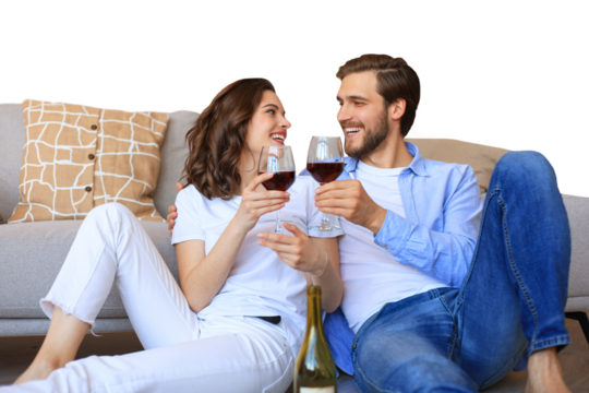 Happy couple sitting, relaxing on floor, drinking red wine. Smiling young husband and wife rest enjoy romantic date on family weekend together on a transparent background