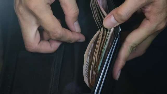 Man's hands holding wallet with Thai baht (THB) cash money banknotes. Concept of saving money for retirement, cash settlement, financial success, literacy and income planning in Thailand.