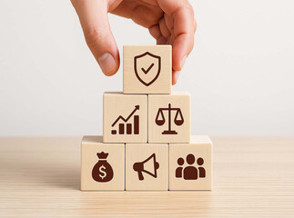Hand arranging wooden blocks with icons of shield graph scale money bag megaphone and group symbolizing protection growth justice finance marketing and teamwork concepts
