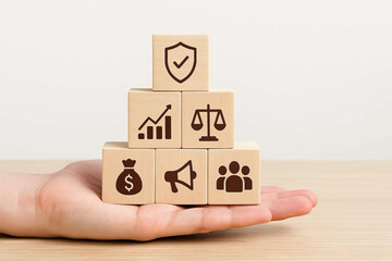 Wooden blocks with business icons stacked on hand, symbolizing growth, security, justice, finance, marketing, and teamwork in balanced and supportive concept