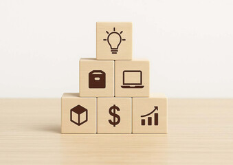 Wooden blocks with business icons including light bulb, box, laptop, cube, dollar sign, and growth chart stacked on wooden surface, symbolizing innovation and financial success