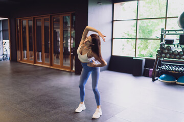 Young woman does dynamic side bend in smart gym, expressing core activation, spinal mobility and...