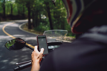 Young male biker using smartphone navigation on parked motorcycle in forest road, exploring with...