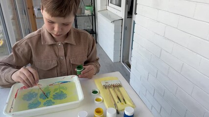 The boy is drawing Ebru art, surrounded by tools on the table, showcasing the significance of creative expression in children's growth.