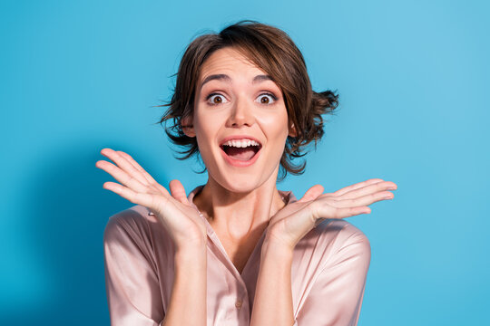Joyful young woman in satin blouse expressing happiness against a vibrant blue background