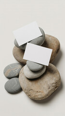 Minimalist flat lay of white business cards balanced on stacked gray river stones with clean white background

