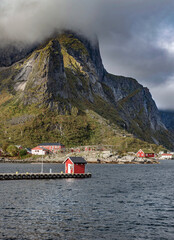 red cabin at the end of a pier at the foot of a Norwegian village and mountain under the clouds on the island of moskenesoya in the archipelago of Lofoten