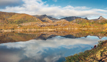 beautiful scenic autumnal landscape with mountaincovered with golden vegetation under the sky reflecting in surface of water in Norway.