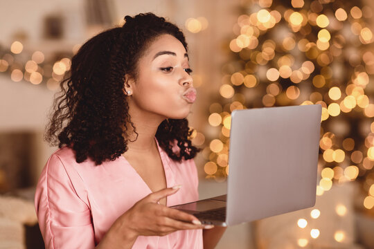 Virtual Or Long Distance Relationship And Online Dating. Portrait of beautiful young curly black woman holding laptop computer in hands and sending kisses to web camera during video chat with partner