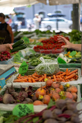Organic vegetables and root crops displayed at farmers market stall, customer hand selecting fresh produce, blurred background with copy space