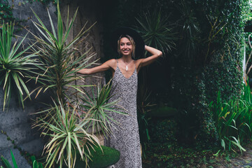 Trendy woman in animal print dress standing confidently among lush plants, embracing creative...