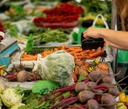 Customer making contactless payment at local farmers market stand filled with colorful fresh vegetables including carrots, beets, lettuce and seasonal produce - Powered by Adobe