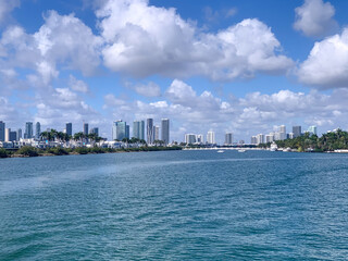 Fototapeta premium A bright, clear view of Biscayne Bay with the modern Miami skyline in the distance. The turquoise water, tropical clouds, and waterfront architecture create a vibrant coastal cityscape