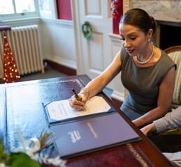 Mid-aged latinamerican woman in grey dress signing marriage ceremony certificate papers at elegant...