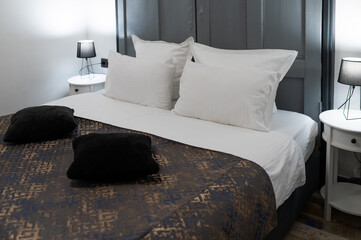 Hotel bed with dark bedspread and white pillows, elegant and inviting atmosphere in a cozy room