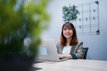 A woman is sitting at a desk with a laptop in front of her. She is smiling and she is happy
