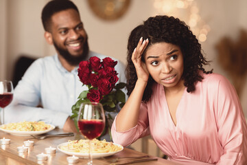 Bad First Impression And Blind Date Concept. Dissatisfied shocked black woman rejecting excited emotional obsessed man who giving her flowers, young couple sitting at table in cafe