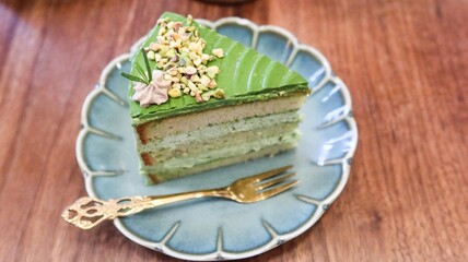 close up of a slice of green pistachio cream cake with layers on a floral plate with copy space on the wooden table 