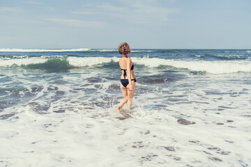 Back view of woman confidently walking deeper into ocean, embracing fearless presence, flow and...