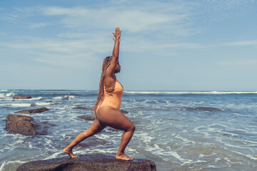 Side profile of woman in warrior pose on sea rock reflects inner discipline, mindfulness and power...