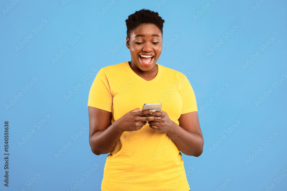Poster Excited African Plus-Size Woman Using Phone Application Standing Over Blue Studio Background. Black Lady Playing Mobile Game On Cellphone. Great App For Your Smartphone Concept
